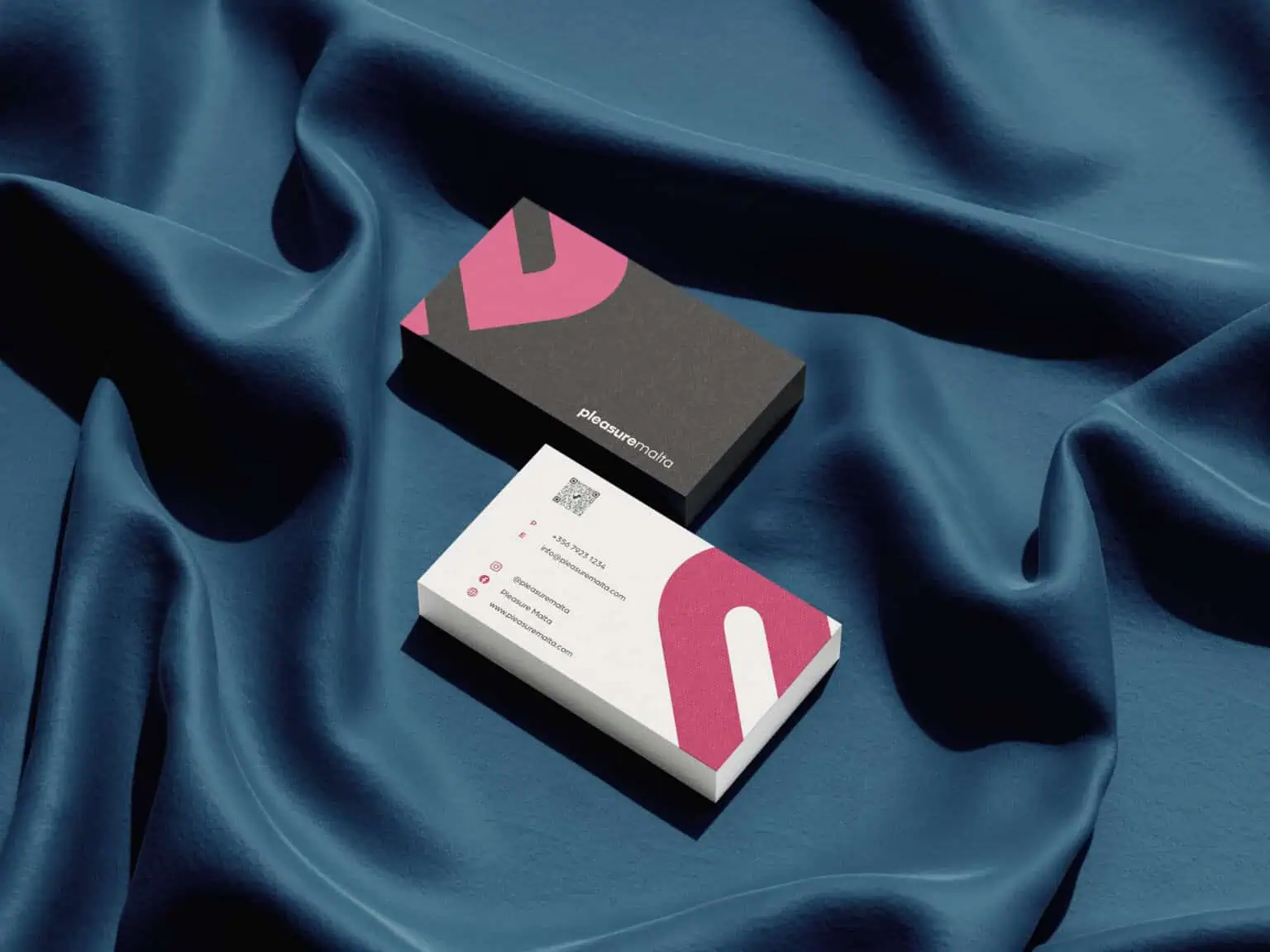 Pleasure Malta Business cards with pastel pink and dark grey design, placed on a silky blue fabric background. The cards feature contact details, social media icons, and a modern aesthetic, suitable for personal or professional use.
