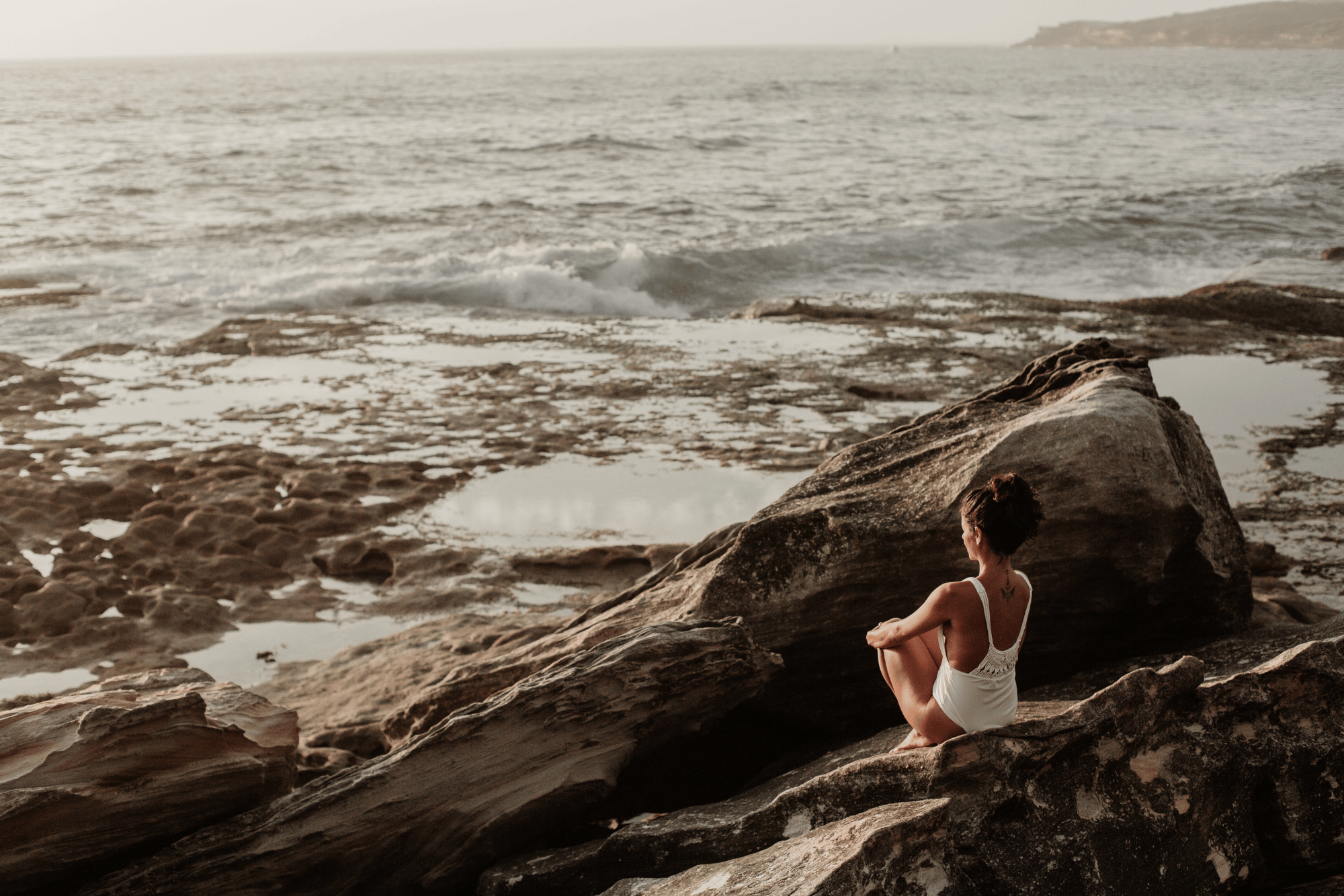 Person sitting down reflecting while facing the sea.