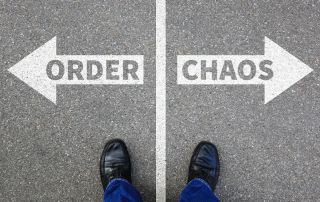 Order instead of chaos concept as a person stands at a crossroads on a street with arrows pointing in opposite directions labeled "Order" and "Chaos".