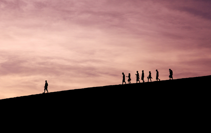 it shows the silhouette of a leader walking and a group of people walking a few steps behind the leader