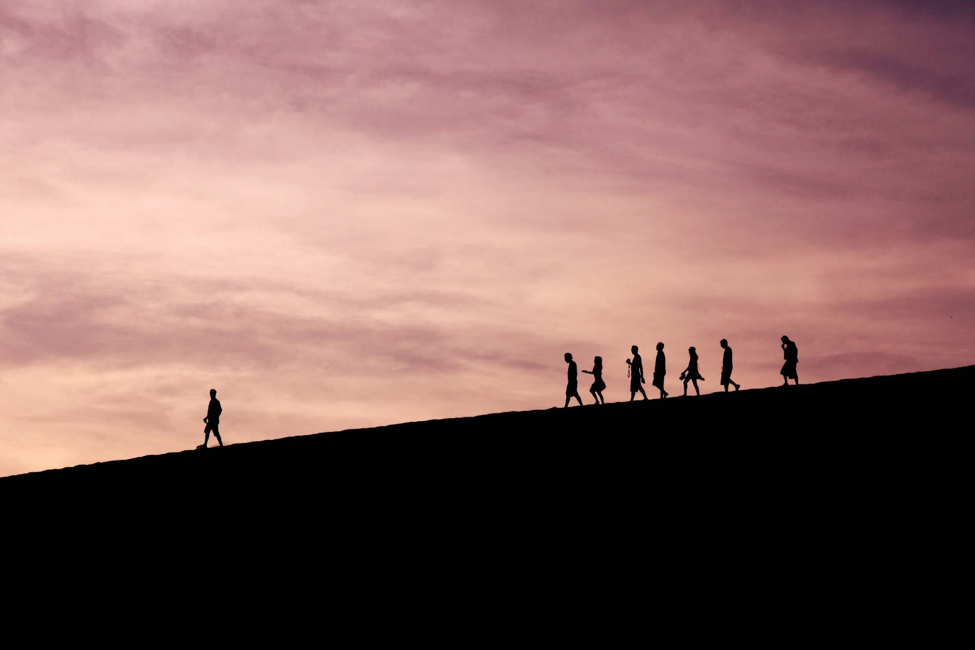 it shows the silhouette of a leader walking and a group of people walking a few steps behind the leader