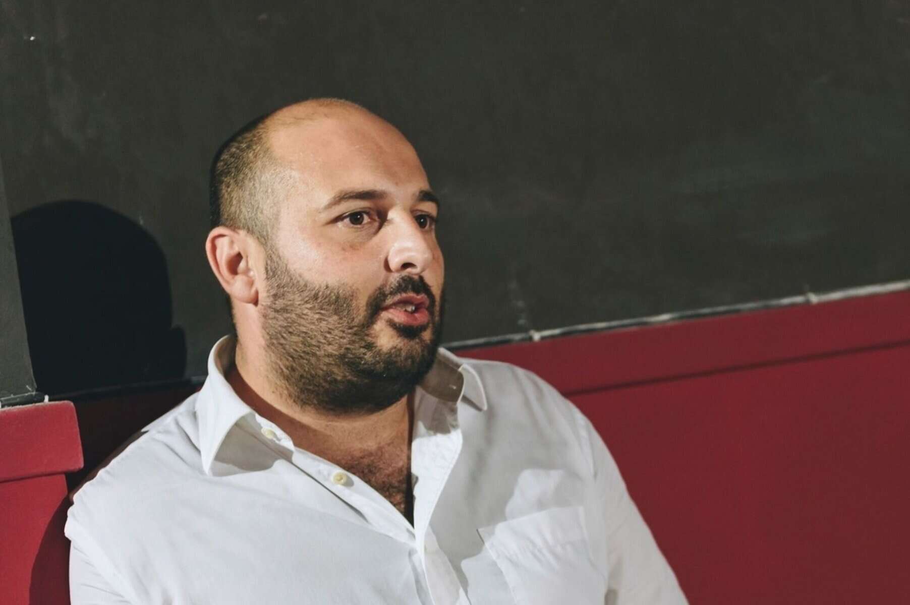 Man speaking in a therapy or counseling session in a clinical setting, focusing on mental health and emotional support, with a serious expression and attentive posture.