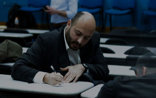 Skeptical man listening during therapy session in dimly lit classroom or conference room, focusing on personal mental health and emotional well-being, professional coaching or counseling environment concise alt text.