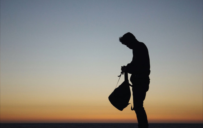 Silhouette of a man holding a bag against a sunset sky, symbolising solitude and reflective leadership.